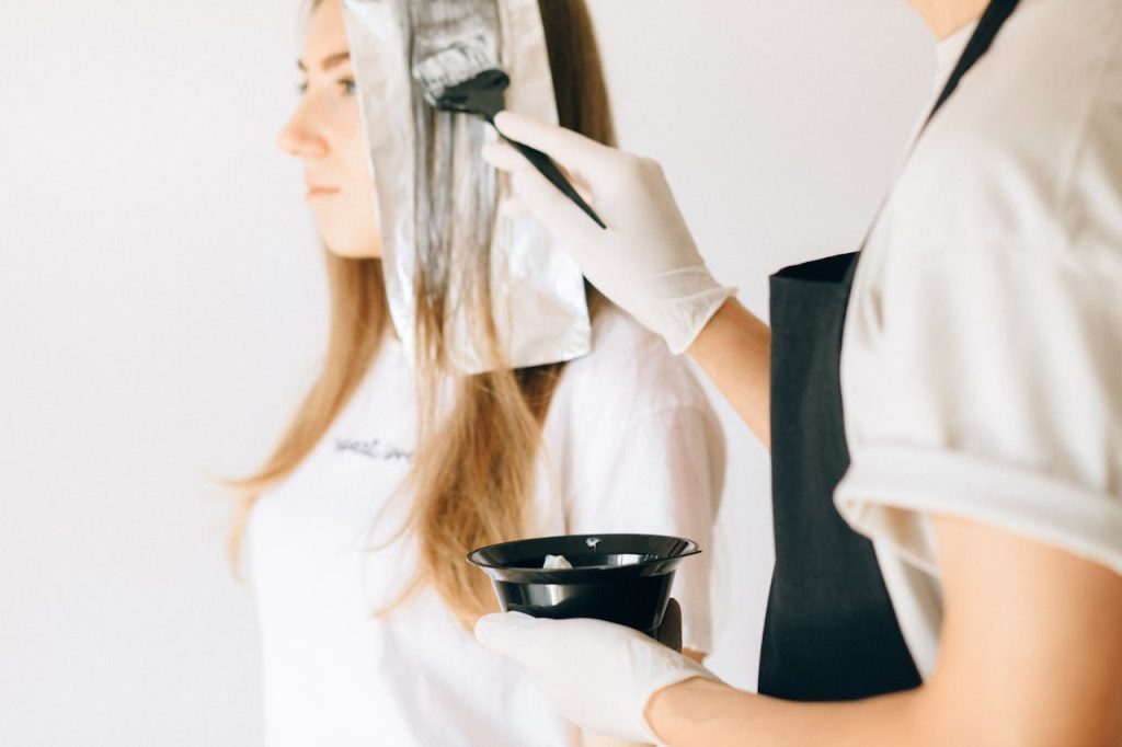 a-hairdresser-coloring-a-woman-s-hair-8468125 Hairdresser applying color to womans hair in salon using brush and foil technique.